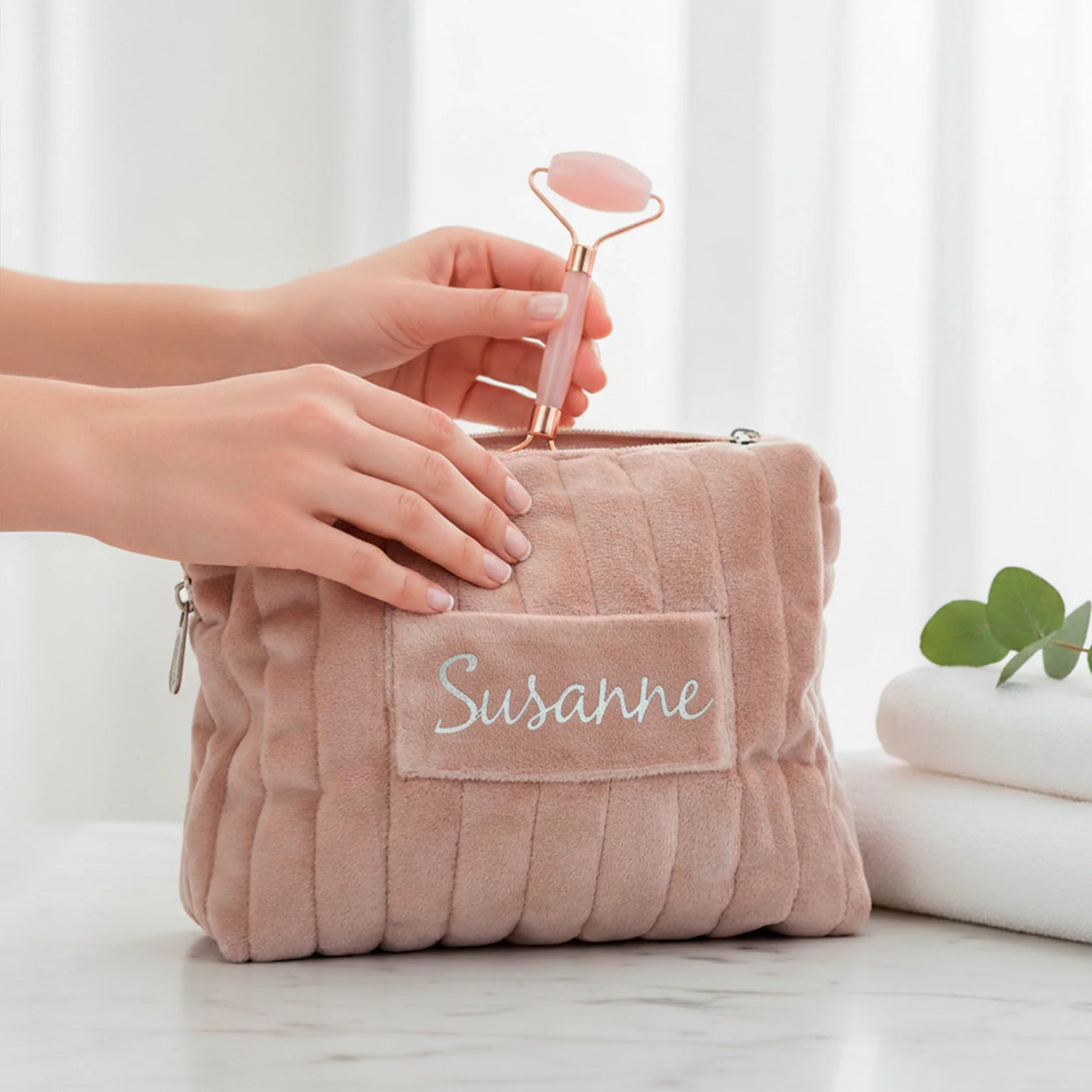Personalized pink plush pouch with name Susanne being held, set on marble, featuring facial roller and towel